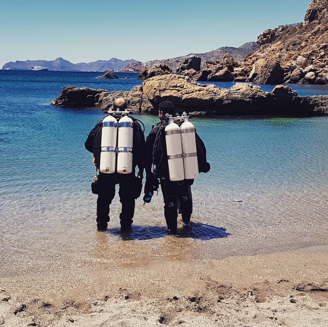 Two divers walking into the water with twinsets